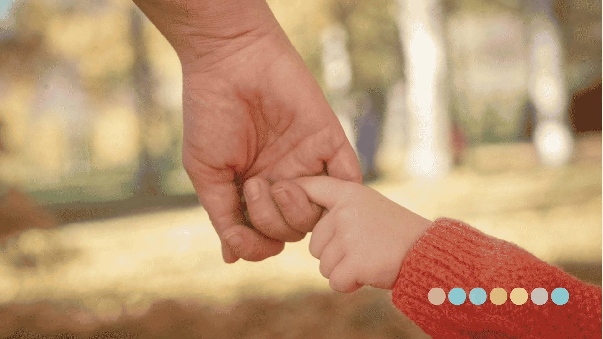 Krupni plan odrasle ruke koja nežno drži malu dečiju ruku u narandžastom rukavu, simbolizujući podršku porodici i detetu sa autizmom.