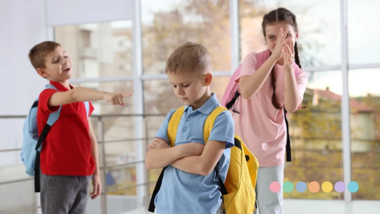 Dečak sa rancem stoji tužno i pognute glave dok ga dvoje vršnjaka u pozadini pokazuju prstom i ismevaju.